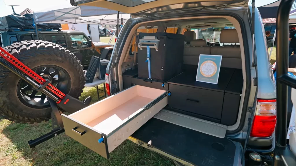 Grand tiroir coulissant ouvert dans le coffre d'un 4x4 à hayon relevé, aménagement overland avec roue de secours